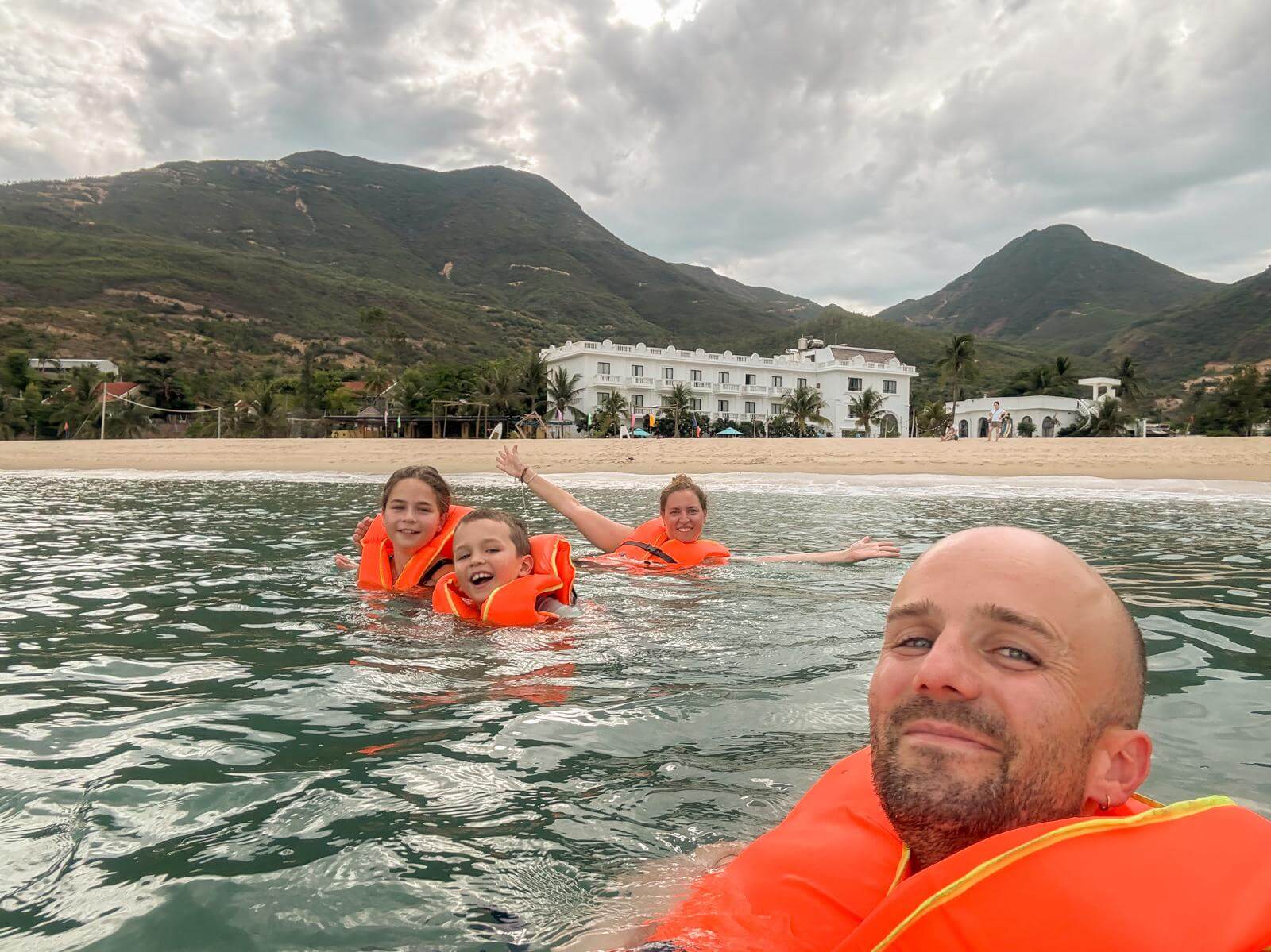 Het hele gezin zwemt met zwemvest in zee, met het resort op de achtergrond