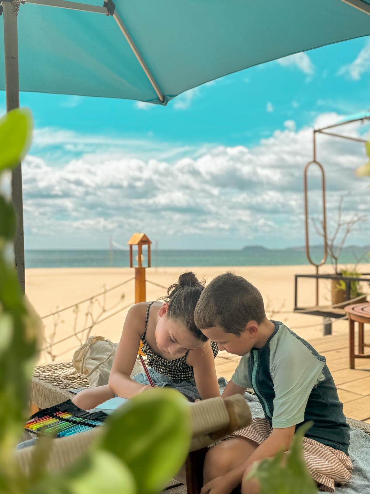 Ida en Otto tekenen samen onder een parasol met zicht op zee